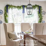 Western red cedar garland accented with blue bows hung around a dining room window..