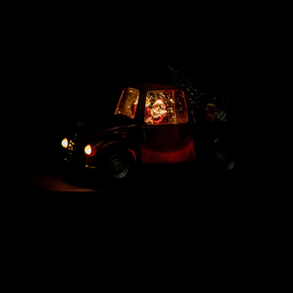 A Lighted Water Globe of Santa driving a truck with a tree, dog, and presents in the back lit up in the dark.