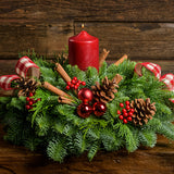 Centerpiece made of noble fir, white pine, incense cedar, red ball clusters, cinnamon-scented Australian pinecones, red and white plaid bows, real cinnamon sticks, red berry clusters, and a red pillar candle up close