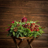 Christmas centerpiece with pine cones, bay leaves, apples and berries and burgundy velveteen bows with a dark wooden background.