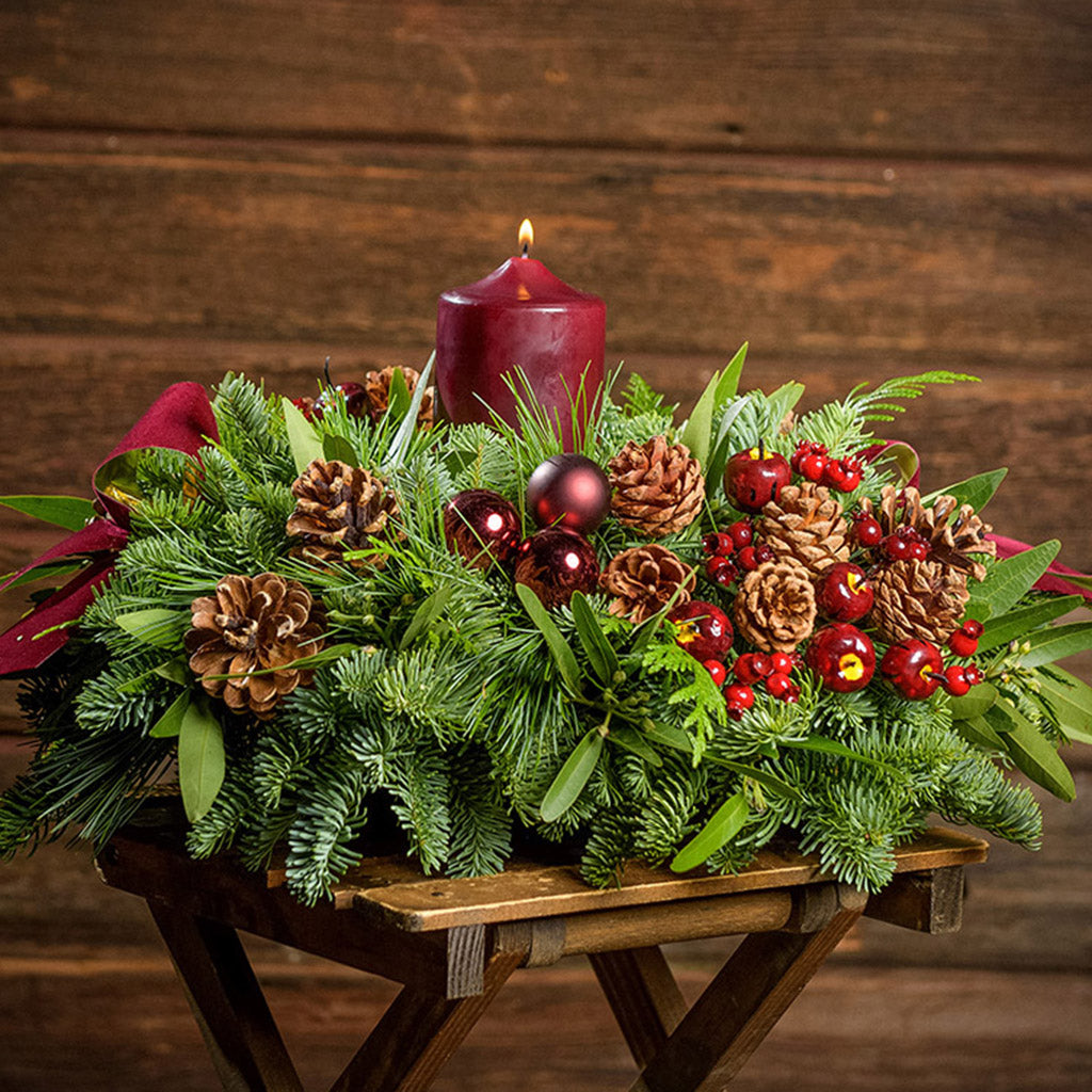 Christmas centerpiece with pine cones, bay leaves, apples and berries and burgundy velveteen bows with a dark wooden background.