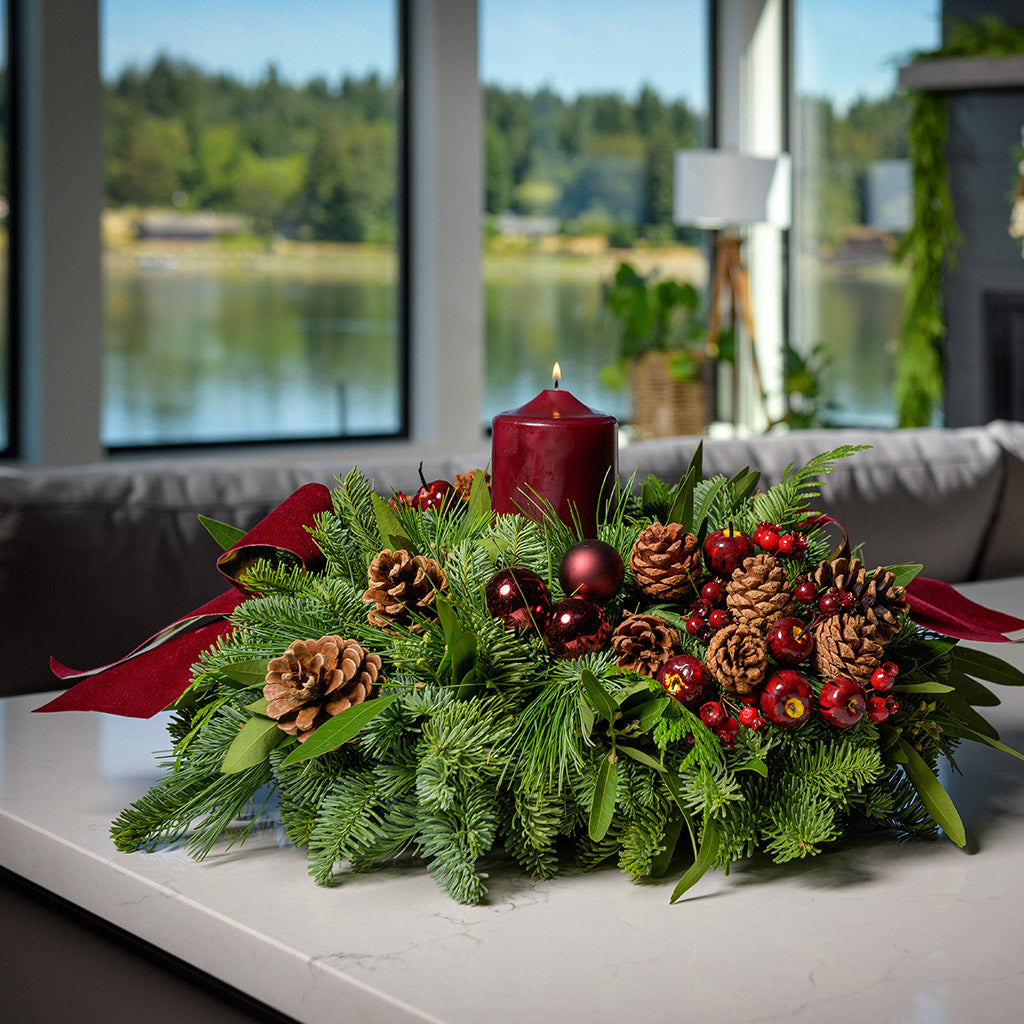 Christmas centerpiece with pine cones, bay leaves, apples and berries and burgundy velveteen bows on kitchen counter