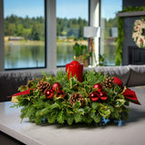 Christmas centerpiece with holly, pine cones, red ornaments and a red pillar candle displayed on a kitchen counter