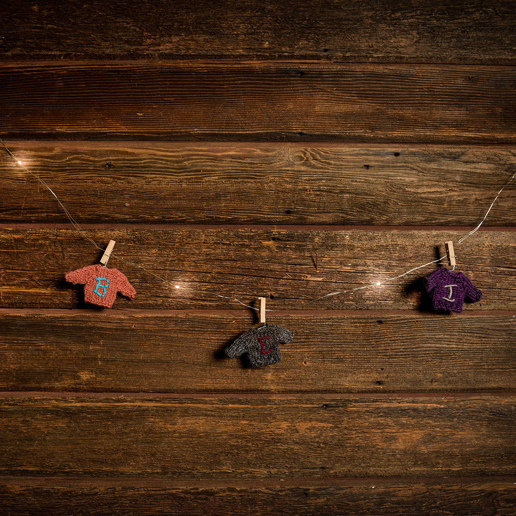 10-foot strand of white lights and sweater ornaments hanging from mini wood clothespins with a dark wooden background.