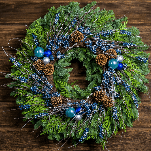 A holiday wreath of noble fir and western red cedar with a ring of faux metallic-blue berries and frosted branches, 3 blue and silver ball clusters, and 8 Australian cones on a wood background.