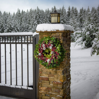 Christmas wreath made of noble fir, cedar, white pine, and bay leaves with 9 frosted Australian pine cones, and a ring of frosted branches with faux burgundy berries hanging on a natural brick pillar.