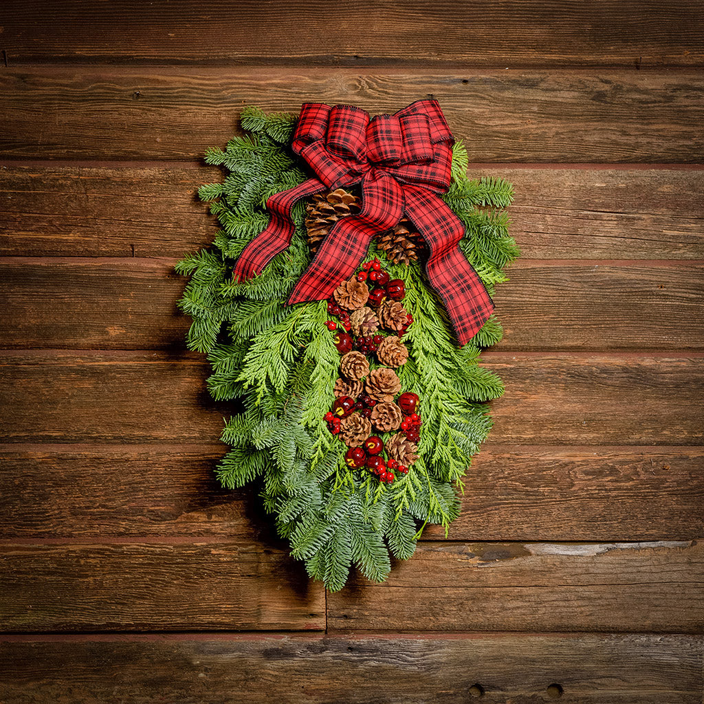 Christmas Swag made with fir cedar juniper pine cone glittery branches silver balls and red and plaid bow on dark wooden background