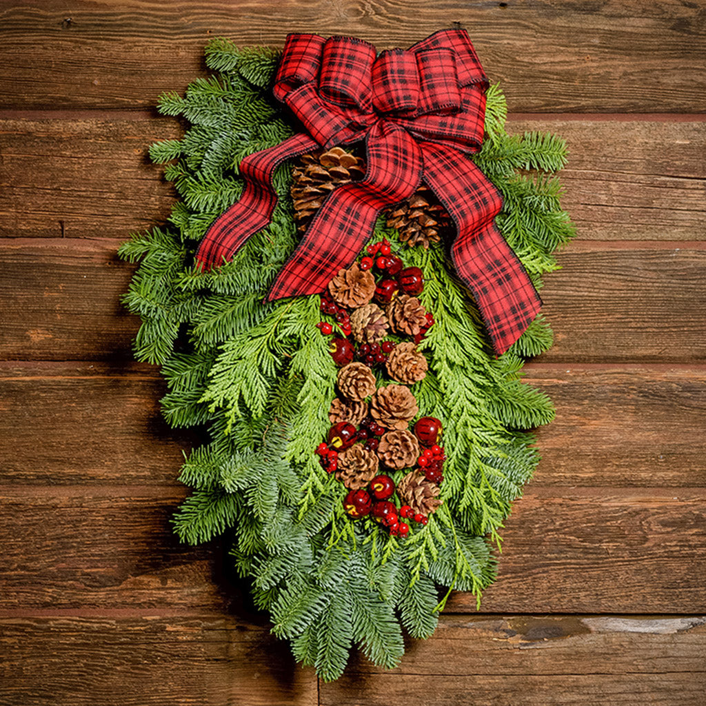 Christmas Swag made with fir cedar juniper pine cone glittery branches silver balls and red and plaid bow on dark wooden background