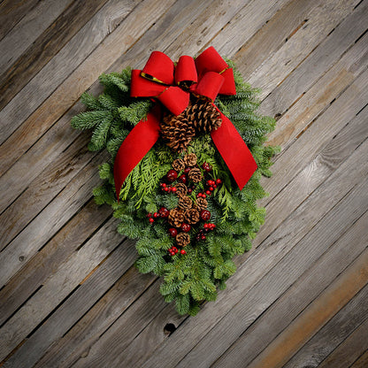 Christmas Swag made with fir cedar juniper pine cone glittery branches silver balls and red bow on light wooden background