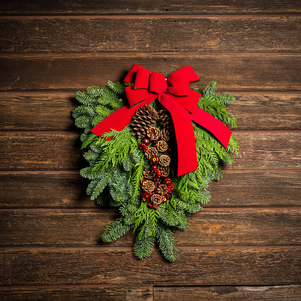 Christmas Swag made with fir cedar juniper pine cone glittery branches silver balls and red bow on wooden background