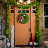 A holiday wreath made of noble fir and white pine with white jingle bells, 3 red berry clusters, 5 Australian pinecones, 2 red ball clusters, and a brushed red linen bow with white edging on a front door accompanied by garland and home decor options.