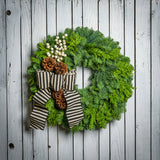 noble fir and cedar with 4 ponderosa pine cones, a branch of faux white berries, and a black and ivory striped burlap bow hanging on a wooden fence