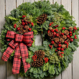 Christmas wreath made with fir, pine, cedar, juniper, pine cones, apples and berries and a red and black plaid bow close up