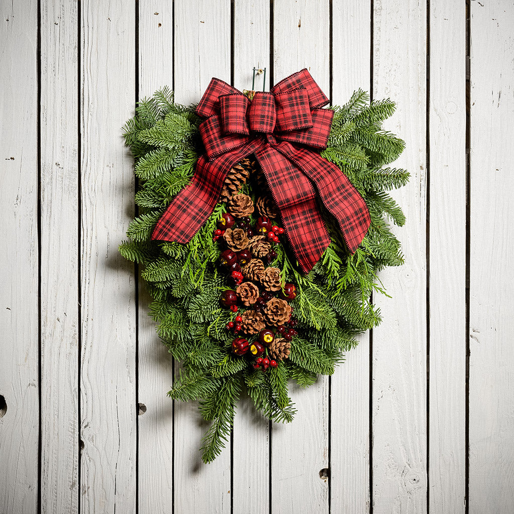 Christmas Swag made with fir cedar juniper pine cone glittery branches silver balls and red and plaid bow on white wooden background
