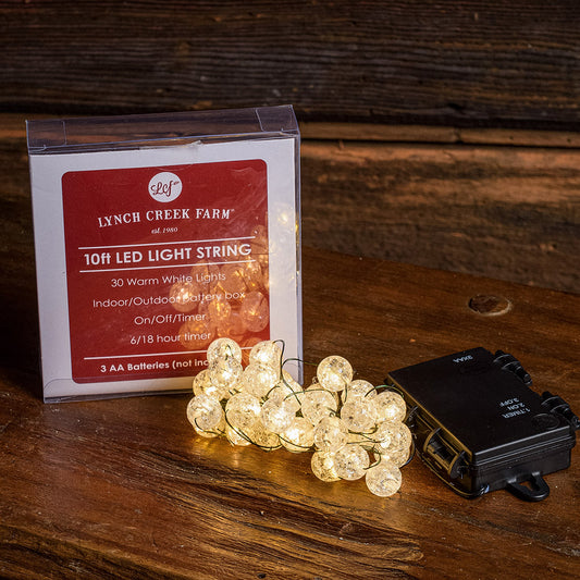 White, globe shaped, cracked glass effect battery operated lights and their packaging with a dark wood background.