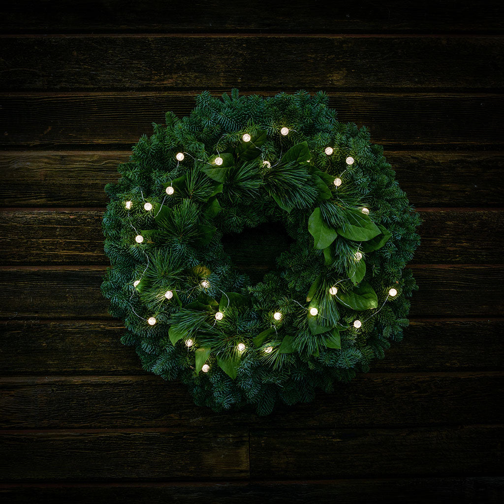 White, globe shaped, cracked glass effect battery operated lights on a evergreen wreath shown illuminated