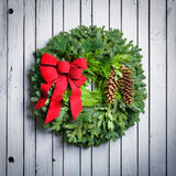 Christmas wreath with bay leaves, pine cones with an red brushed linen bow on a white wood background.
