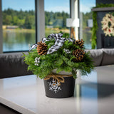 An arrangement made of noble fir, incense cedar, and white pine with Austrian pinecones, silver berry clusters, and a black and white plaid bow, black and white metal container, and white snowflake sitting on a counter.