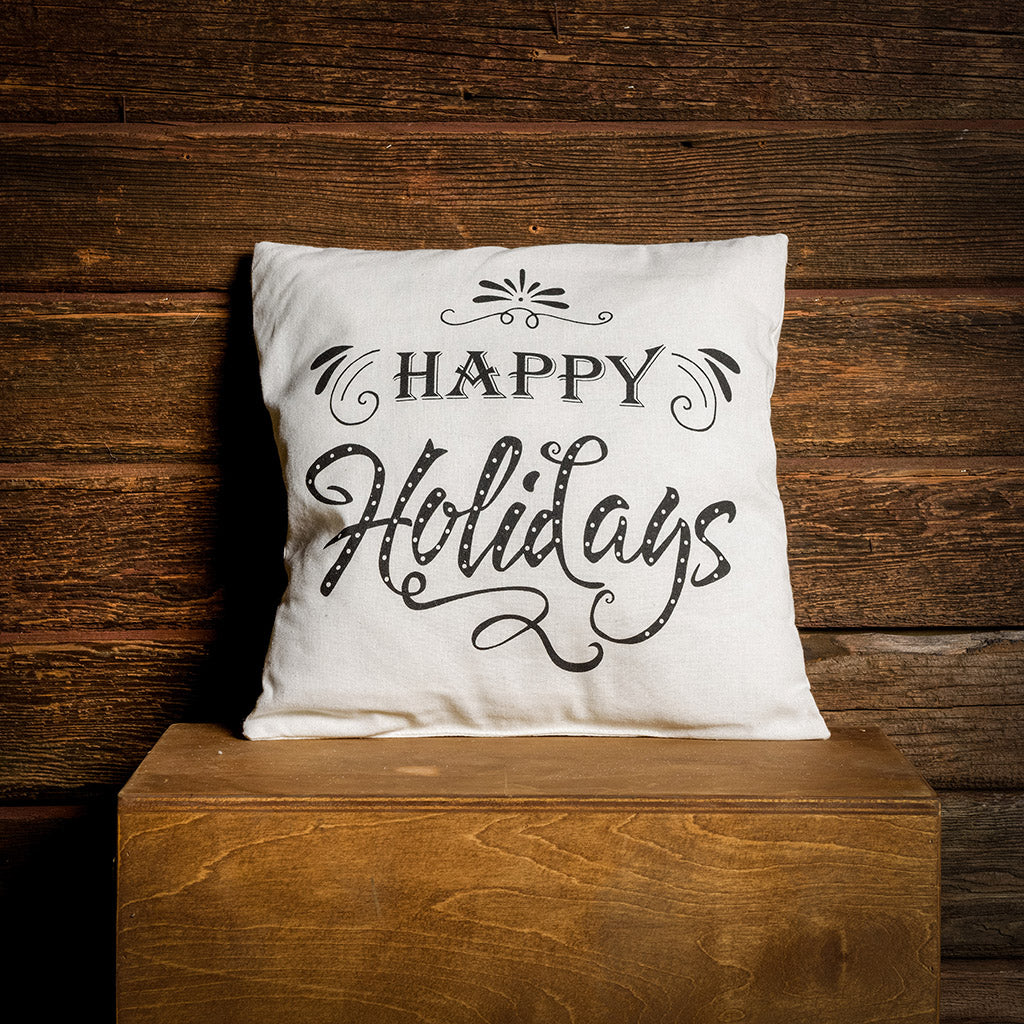 Happy Holidays accent pillow in cream with black lettering on a wooden background. 
