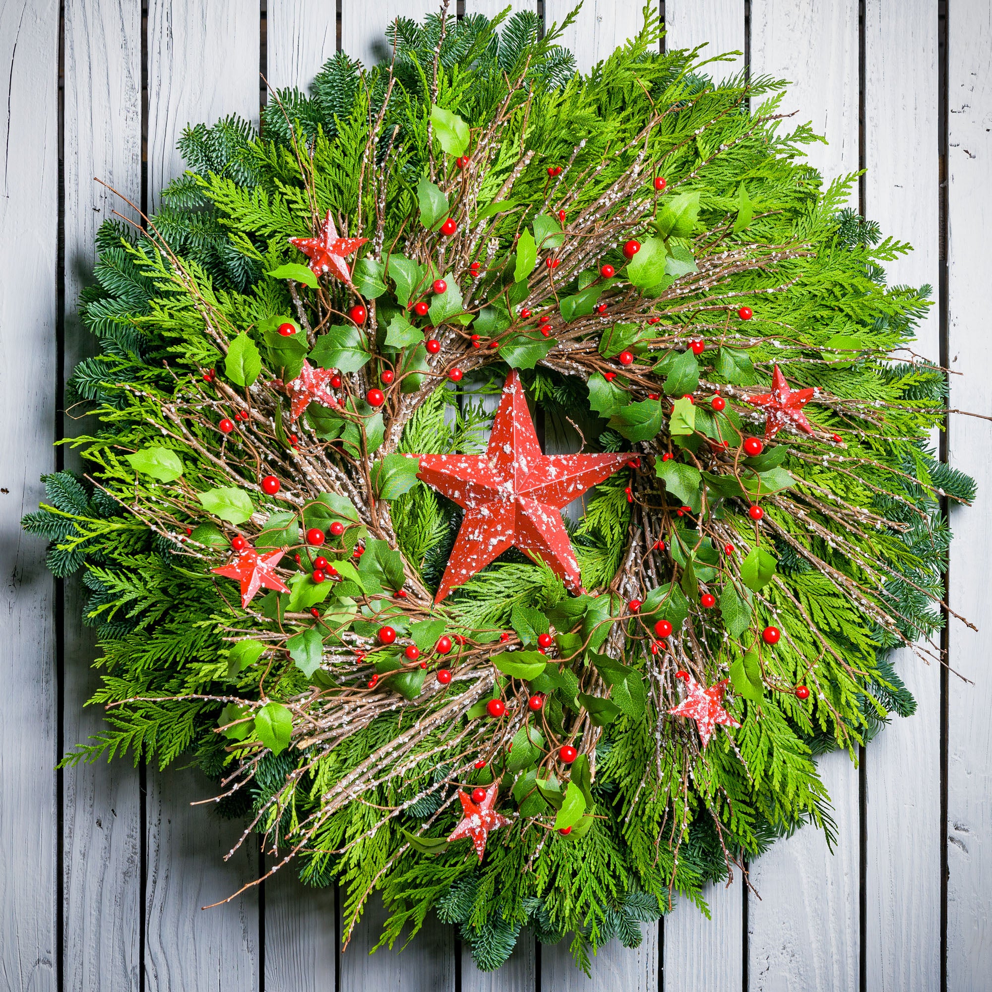 Farmhouse holiday Christmas wreath with speckled red, rustic stars, berries, holly and twigs on a base of noble and cedar