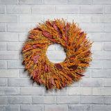Burgundy salal leaves, dijon oats, orange phalaris, natural flax, and red flax are perfectly blended in to a 22" wreath on a white brick background. 