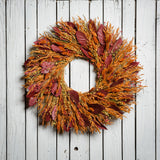 Burgundy salal leaves, dijon oats, orange phalaris, natural flax, and red flax are perfectly blended in to a 22" wreath on a white wood fence background. 