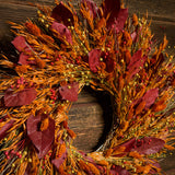 Burgundy salal leaves, dijon oats, orange phalaris, natural flax, and red flax are perfectly blended in to a 22" wreath on a dark wood background. 