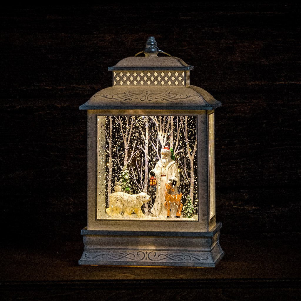 A Lighted Water Globe in white of Father Christmas with forest animals and snow-covered trees lit up with a dark background.