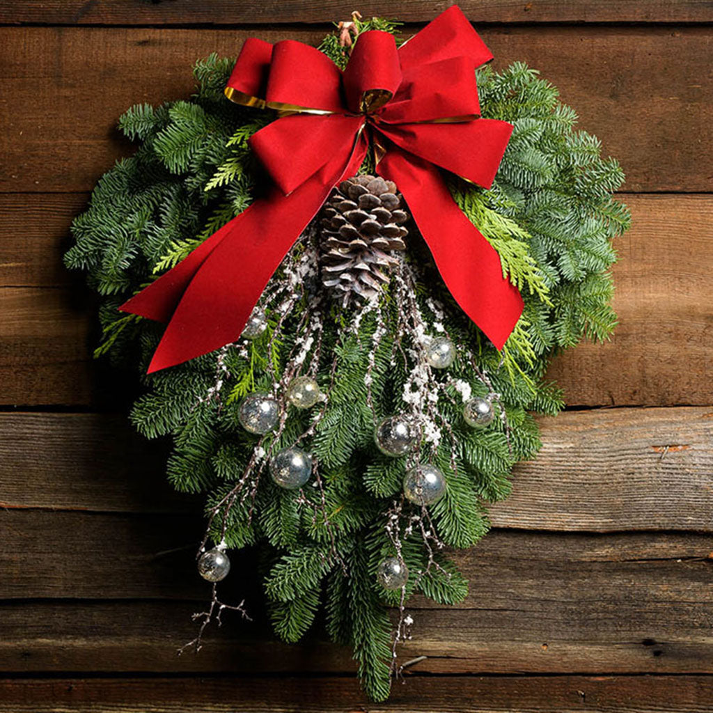 Christmas Swag made with fir cedar juniper pine cone glittery branches silver balls and red bow on wooden background