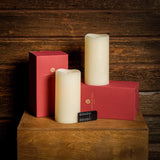 Set of 2 ivory colored LED candles and their packaging and remote with a dark wooden background.