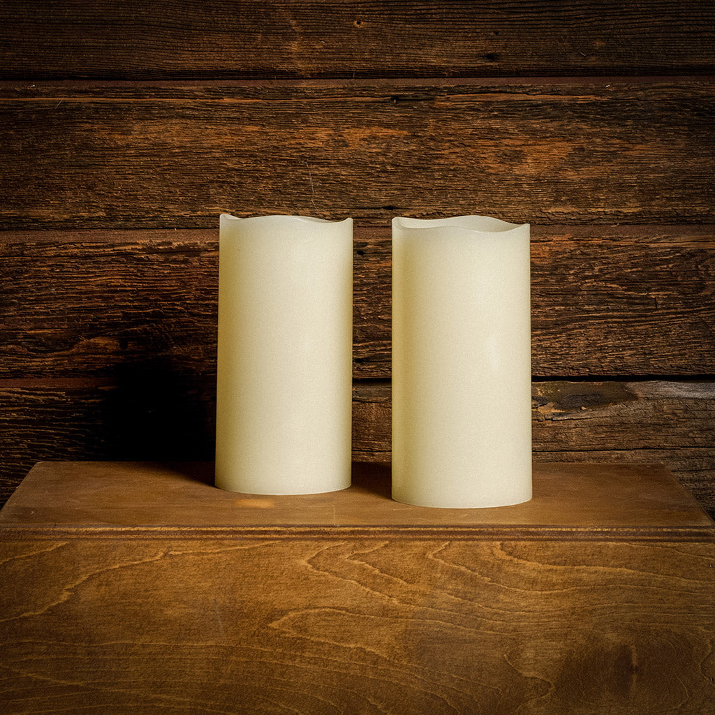 Set of 2 ivory colored LED candles with a dark wooden background.
