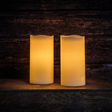 Set of 2 ivory colored LED candles lit with a dark wooden background.