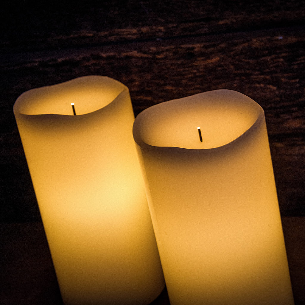 Set of 2 ivory colored LED candles lit with a dark wooden background.