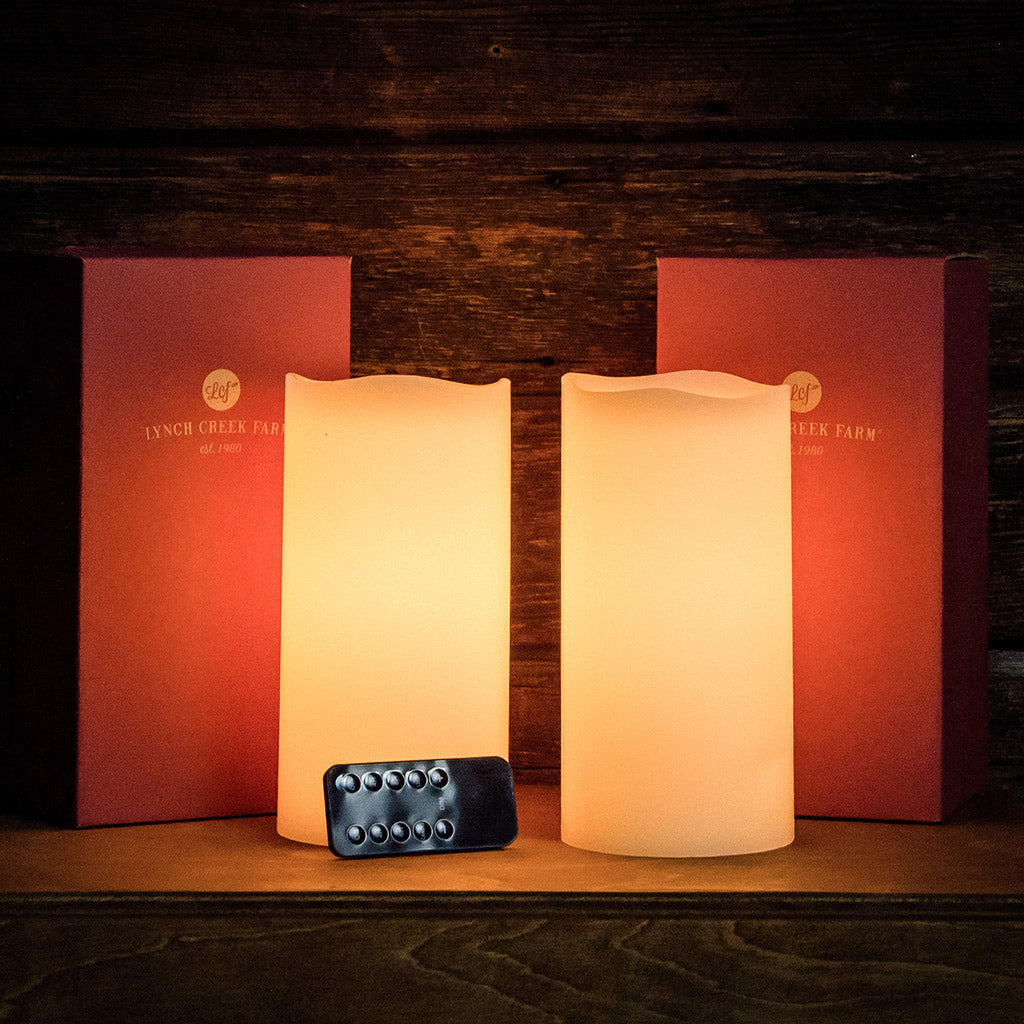 Set of 2 ivory colored LED candles lit and their packaging and remote with a dark wooden background.