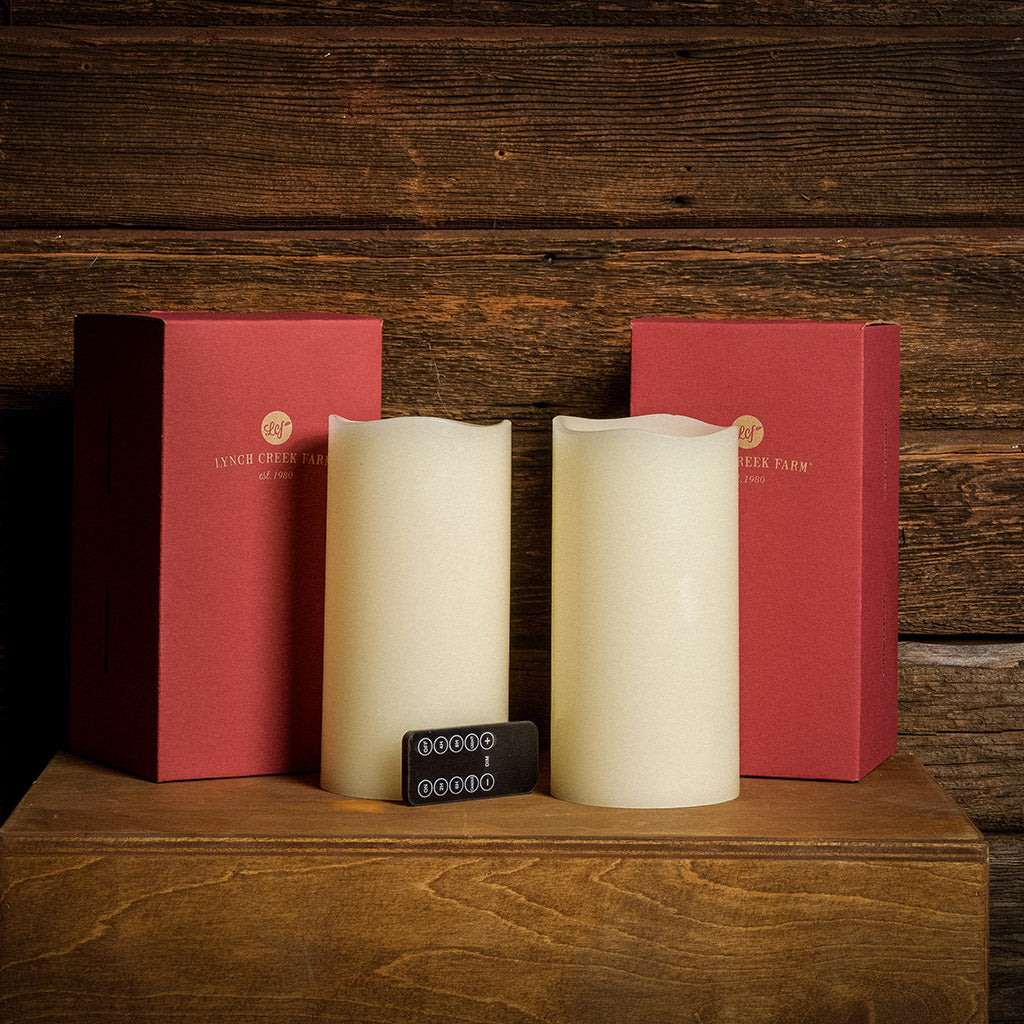 Set of 2 ivory colored LED candles and their packaging and remote with a dark wooden background.