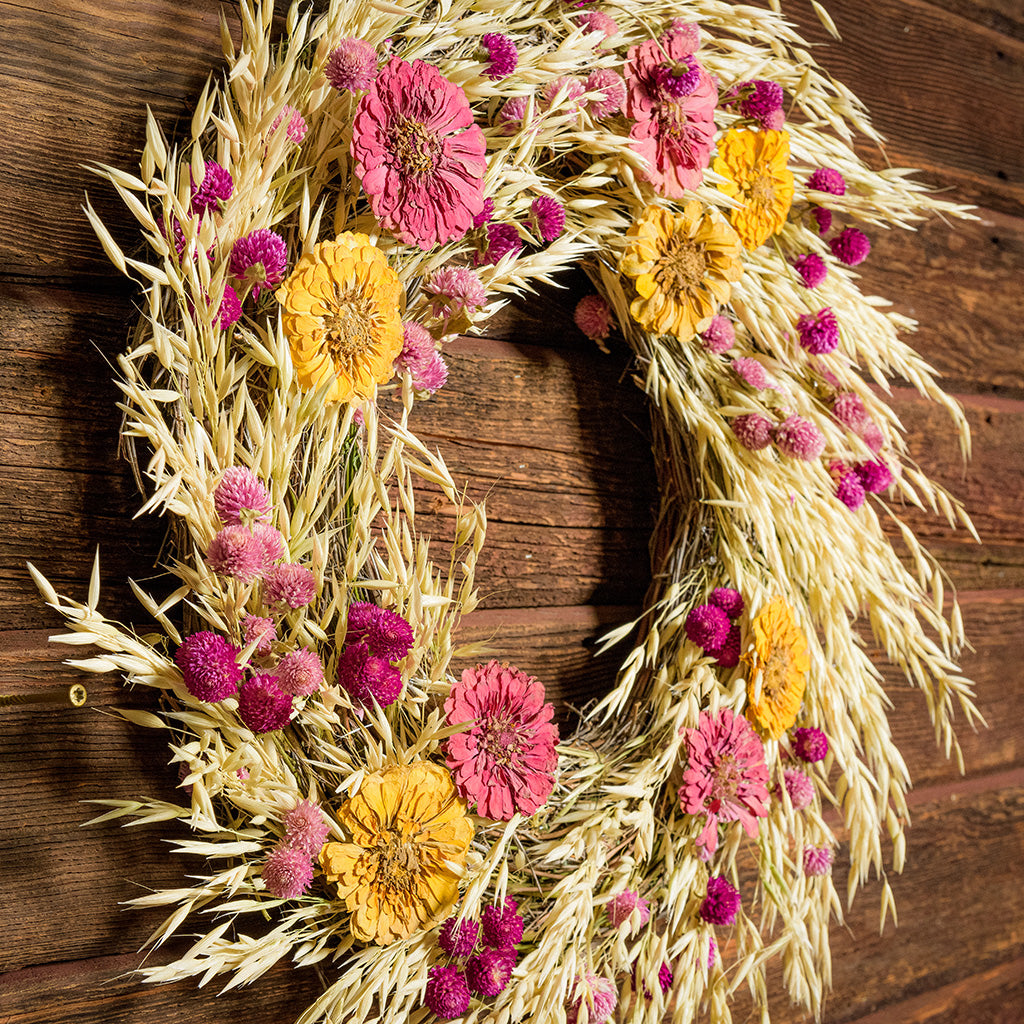 22" wreath made of purple globe amaranthus and Avena oats, along with the sweet zinnia flowers on a dark wood background. 