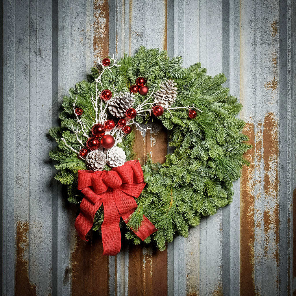 Christmas wreath made with noble fir, pine, pine cones, snow-covered branches, red balls and a red burlap bow