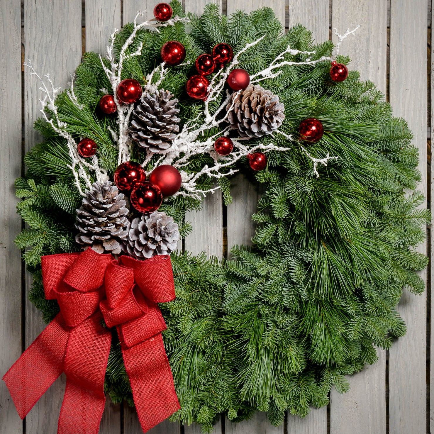 Christmas wreath made with noble fir, pine, pine cones, snow-covered branches, red balls and a red burlap bow close up