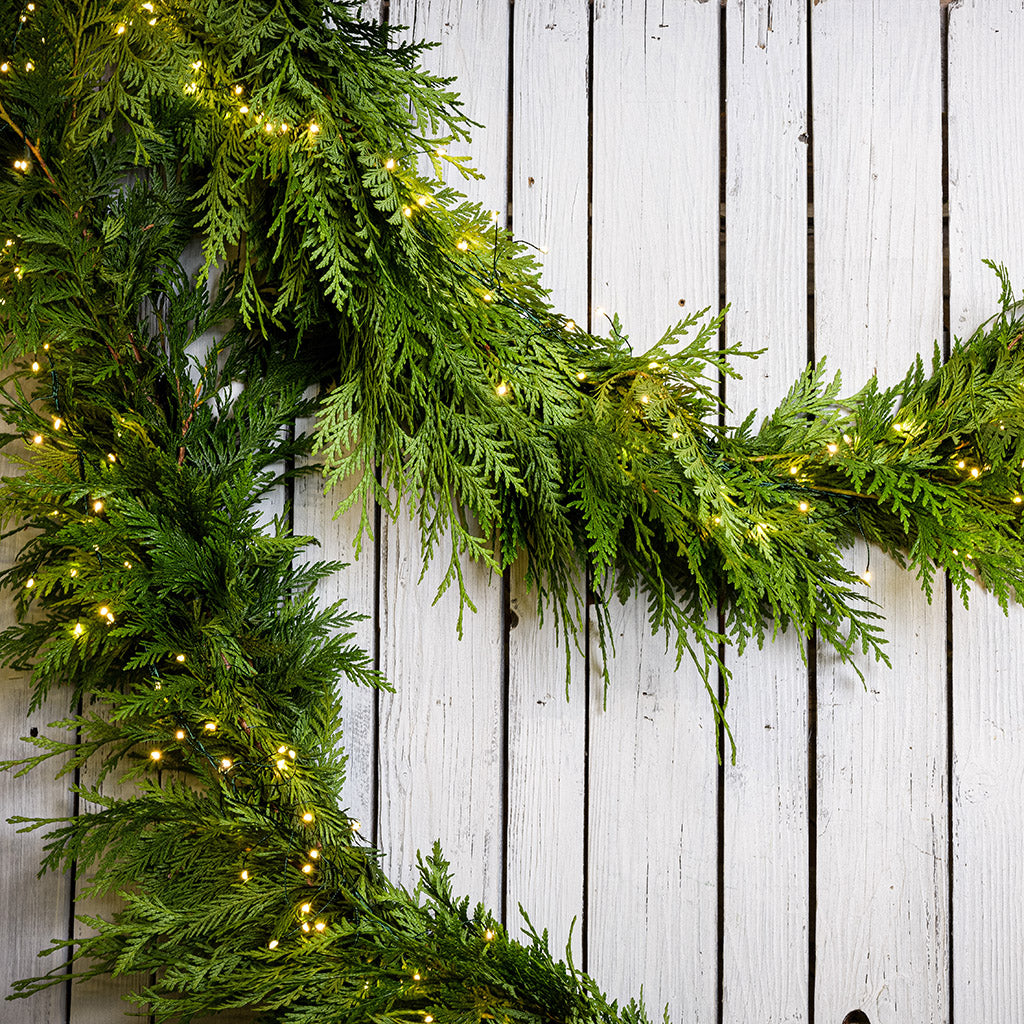 White, uniquely-shaped, battery operated lights on cedar garland with a white wood background.