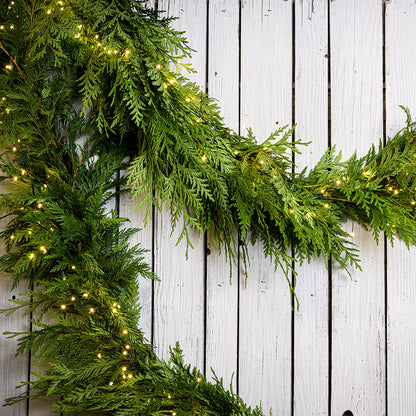 White, uniquely-shaped, battery operated lights on cedar garland with a white wood background.