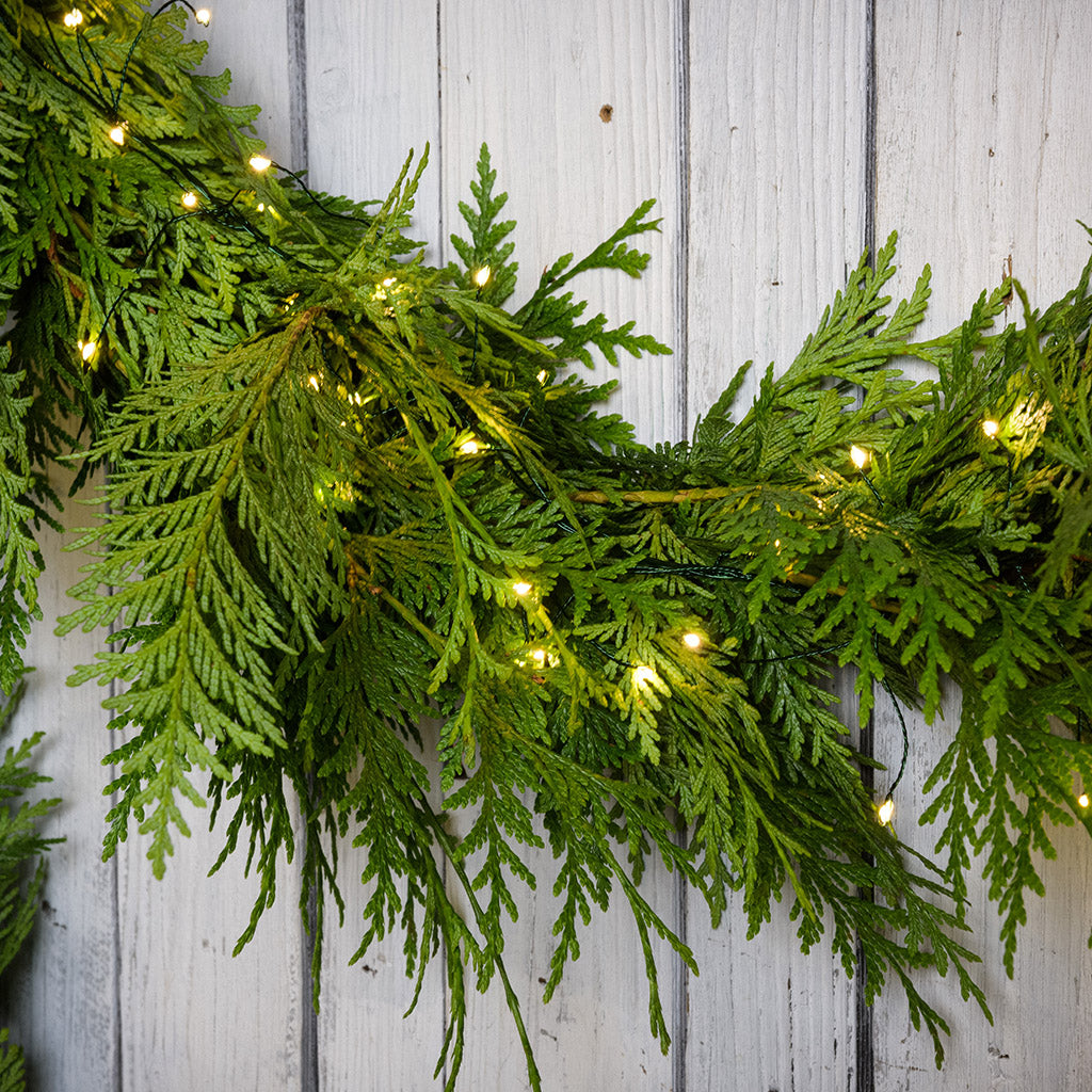White, uniquely-shaped, battery operated lights on cedar garland with a white wood background.