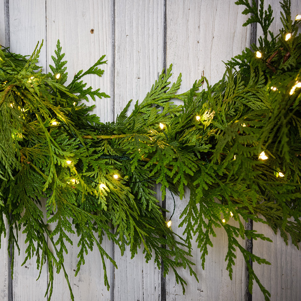 White, uniquely-shaped, battery operated lights on cedar garland with a white wood background.