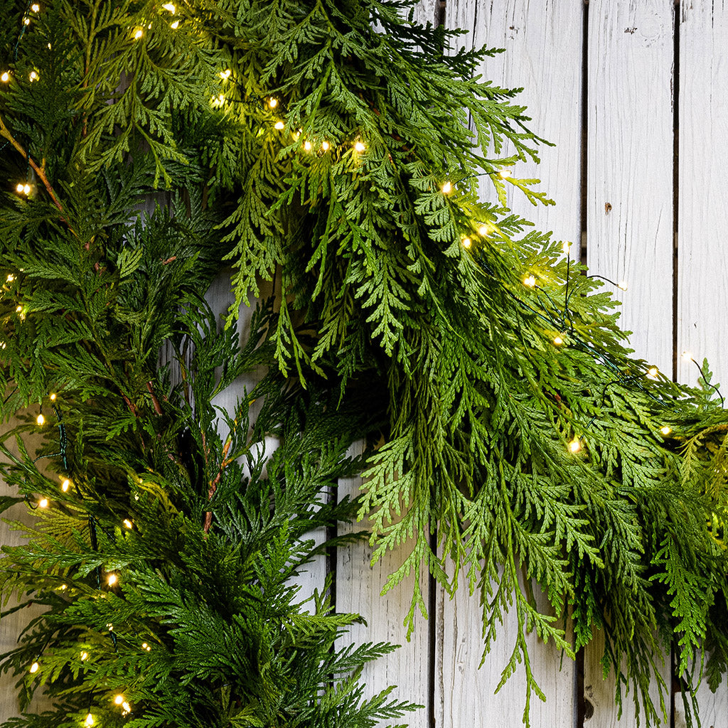 White, uniquely-shaped, battery operated lights on cedar garland with a white wood background.