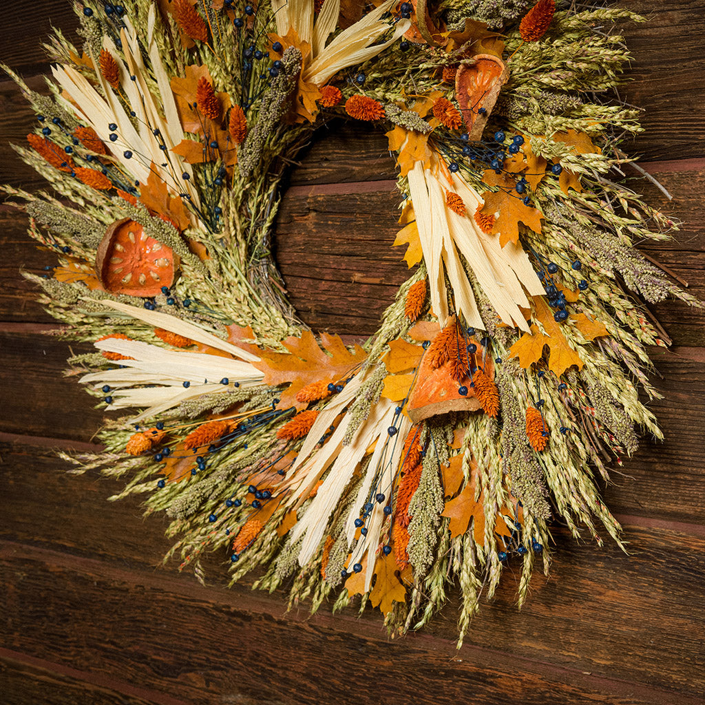 22" wreath made of corn husk, phalaris, natural flax, maple leaves, and dried quince slices on a dark wood background. 