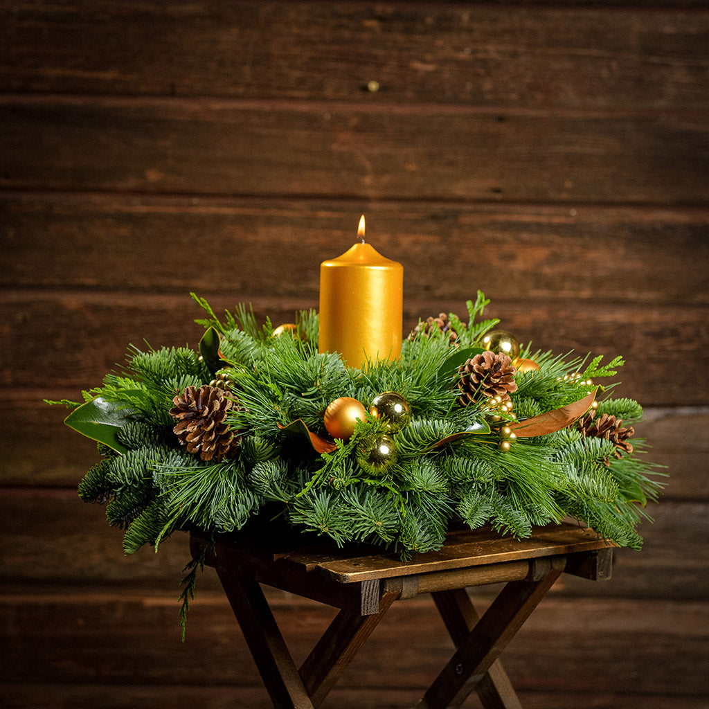 Golden magnolia centerpiece with pine cones, magnolia, gold balls and berries and a golden pillar candle with a dark wooden background.