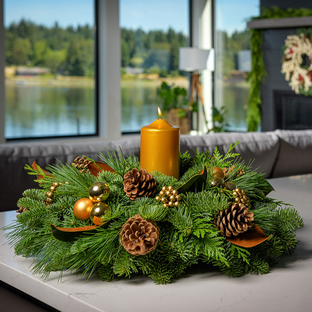 Golden magnolia centerpiece with pine cones, magnolia, gold balls and berries and a golden pillar candle on kitchen counter