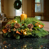Golden magnolia centerpiece with pine cones, magnolia, gold balls and berries and a golden pillar candle on kitchen counter