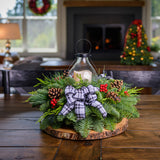 Centerpiece made of noble fir, cedar, and pine with Australian pine cones, red berry clusters, a black and white plaid bow, and an old schoolhouse-style metal LED displayed on a wooden table