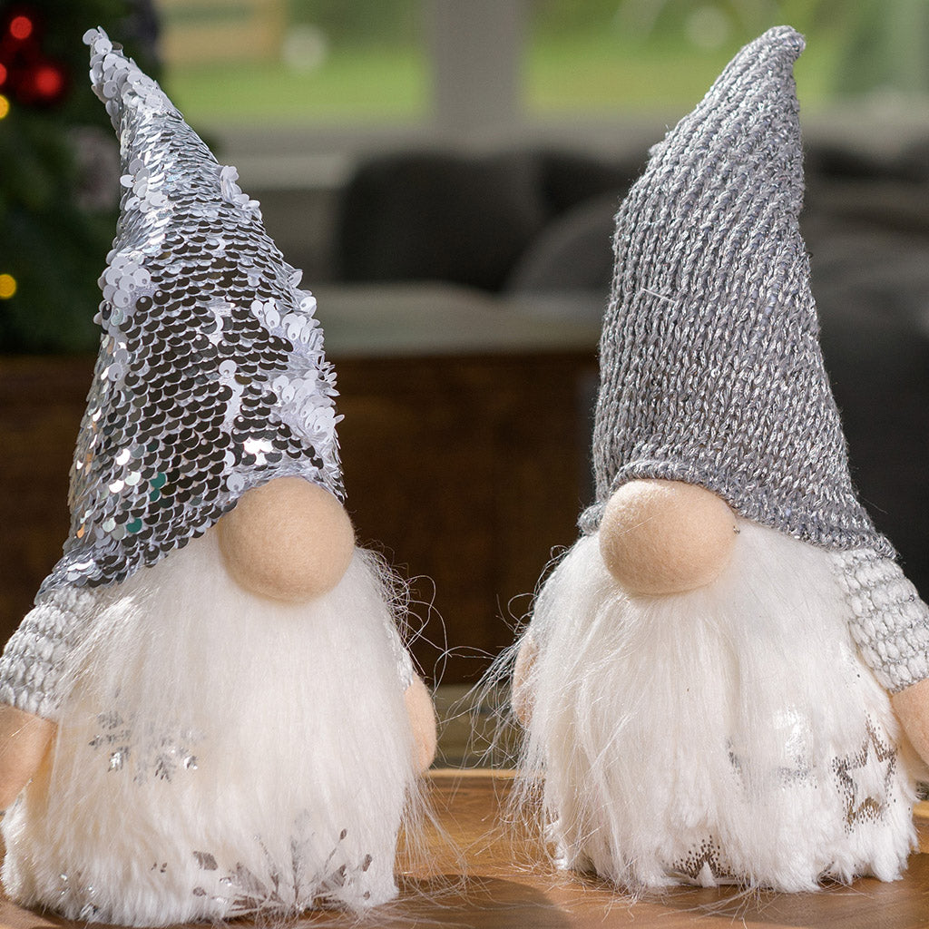 Sparkling winter light-up gnomes in fuzzy white outfits and pointy hats sitting on a table.