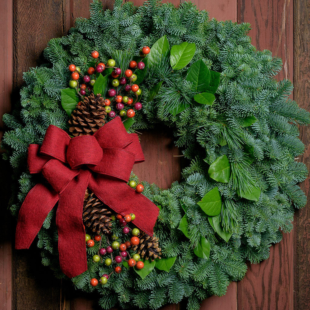Holiday wreath with pine cones, faux autumn berries and a red linen bow on a base of noble, pine and salal greens